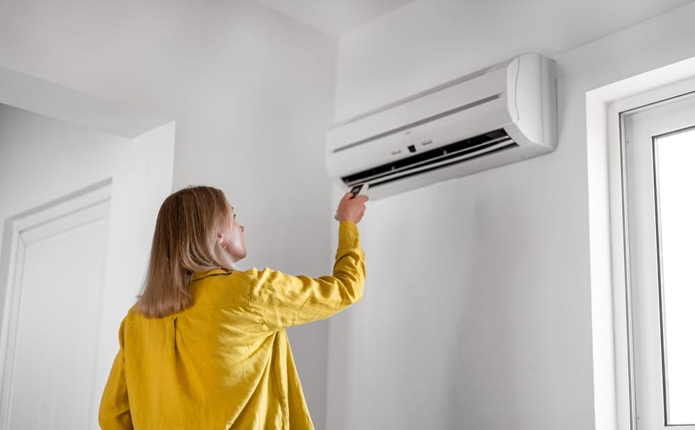 Woman holding remote control aimed at the air conditioner. 
