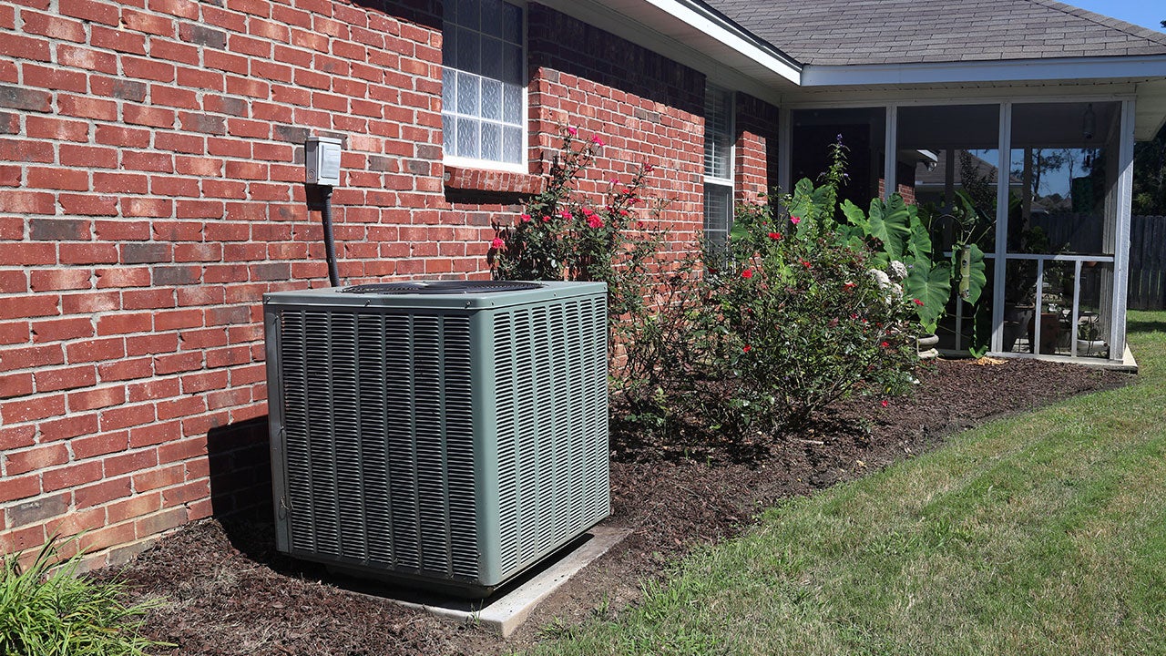 A view of outdoor AC unit next to brick house with garden and lawn
