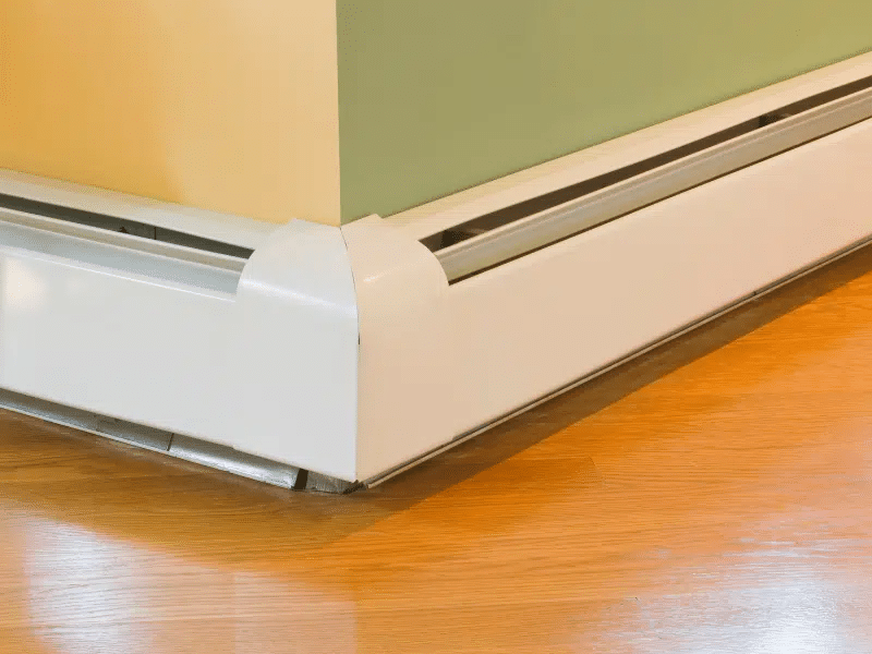 Corner view of a white baseboard heater on wood flooring