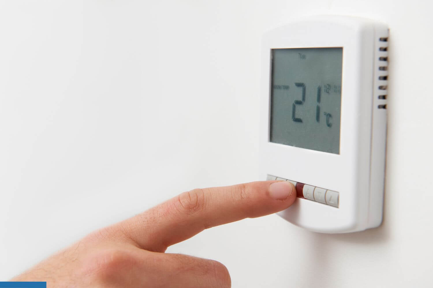 Finger pressing a button on a digital wall-mounted thermostat displaying 21°C