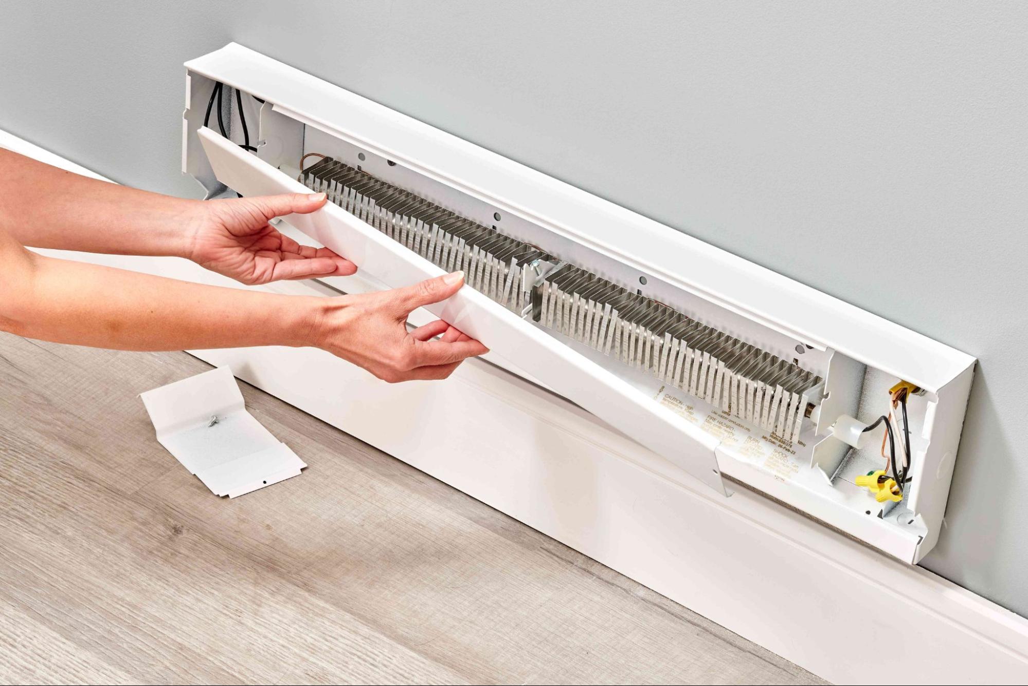 Person removing the front cover of an electric baseboard heater for maintenance or cleaning