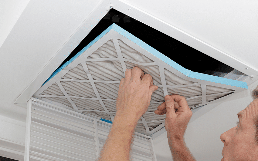 Person replacing an air filter in a ceiling vent as part of HVAC system maintenance