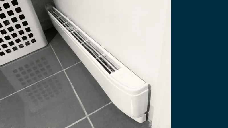 Slim white baseboard heater installed along a tiled floor wall, next to a laundry basket