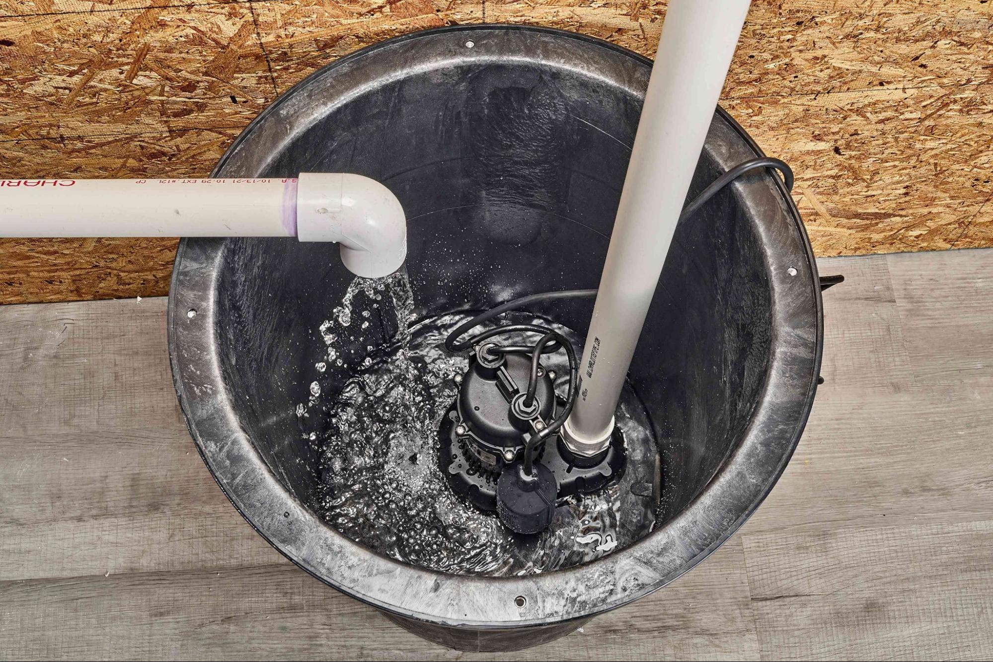 Sump pump draining water through a PVC pipe in a basement pit