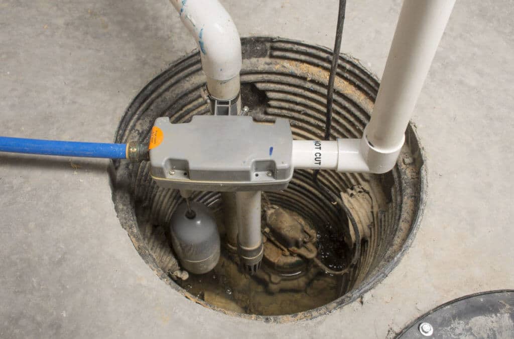 Sump pump setup in a basement pit with discharge pipes, a float switch, and a backup system connected