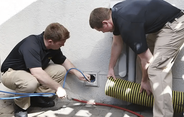 Two technicians cleaning an outdoor dryer vent using a vacuum hose and compressed air tools_11zon