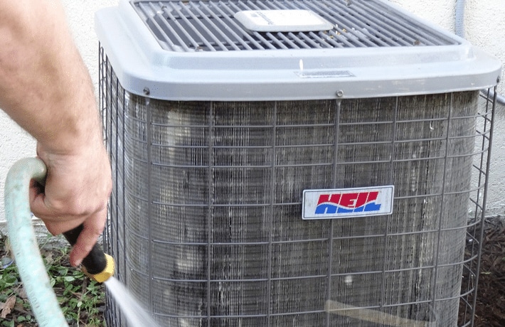 close-up of a hand cleaning condenser coils outside