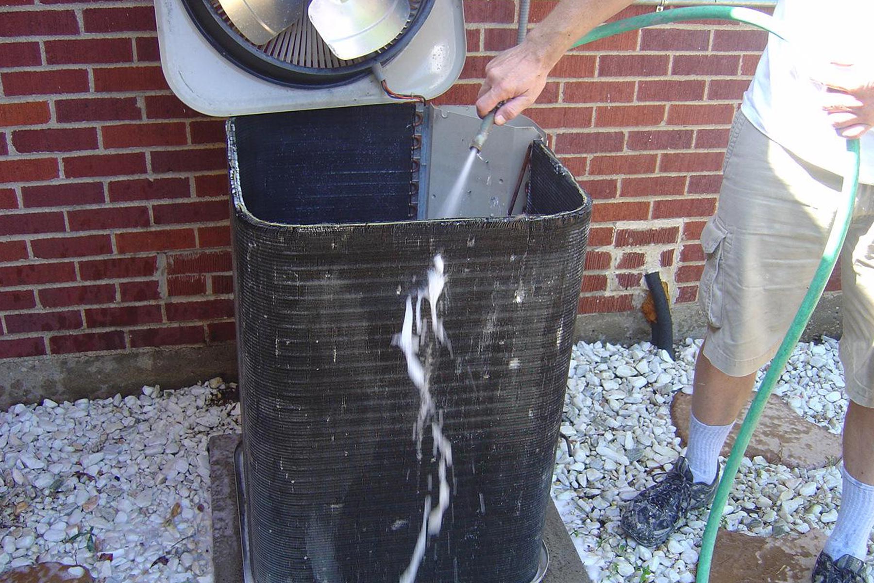 zoomed view of hands cleaning condenser coils with a pipe